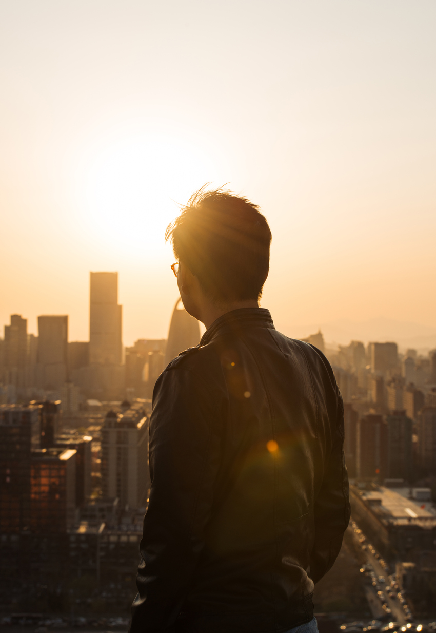 A person looking over a city skyline as the sun is heading towards the skyline