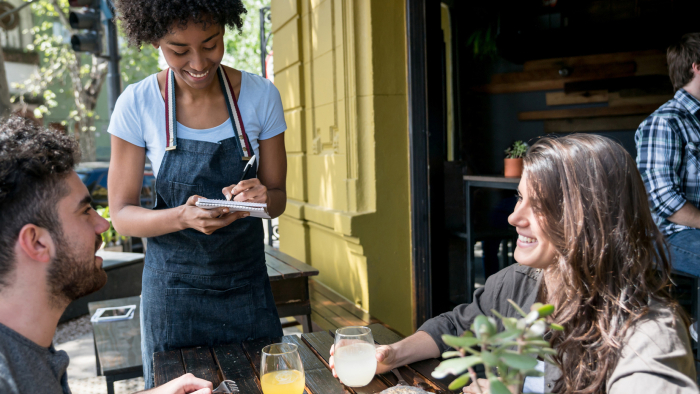 Waitress taking the order of two people sitting outdoors at a restaurant 