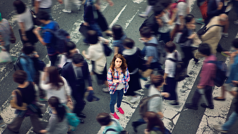 One person in focus, looking at the camera, in a busy cross walk, many other people walking by out of focus