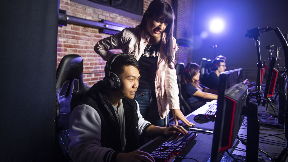 a female esports coach watching and helping a male gamer
