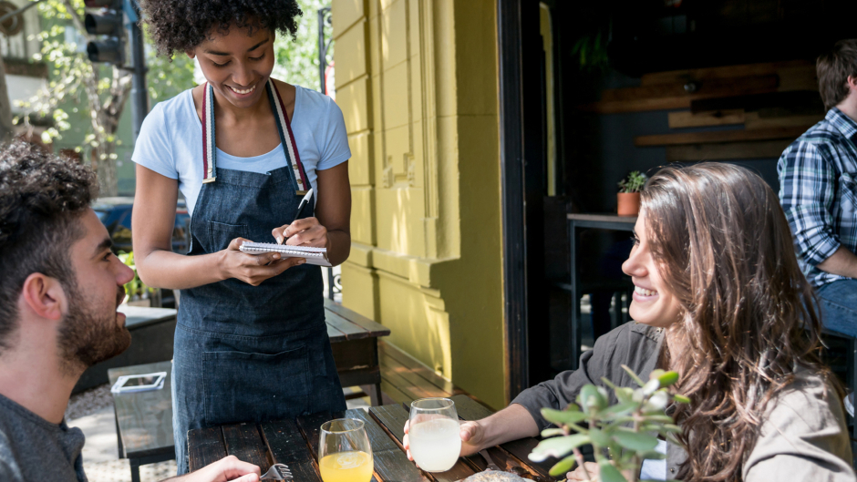Waitress taking the order of two people sitting outdoors at a restaurant 