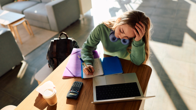 Person overwhelmed by studying. lots of study materials spread out on desk